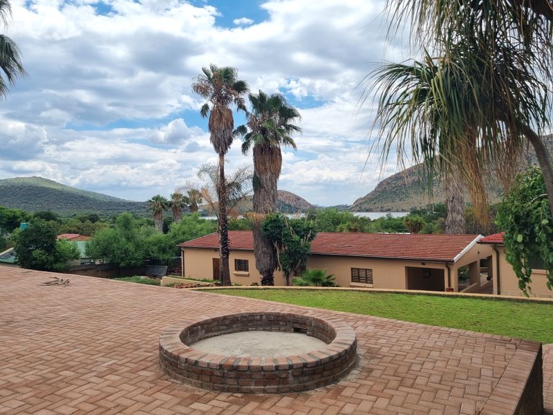 Spacious brick-paved patio featuring a built-in circular brick fire pit, overlooking a landscaped garden with scenic mountain and water views.