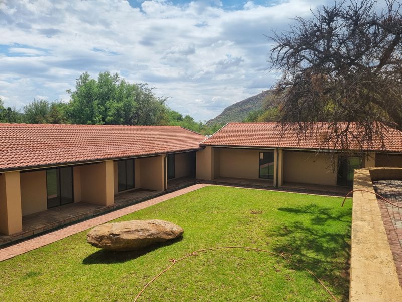 A well-maintained rear exterior view of the guest house featuring a central lawn, covered patio areas, and terracotta tiled roofing.