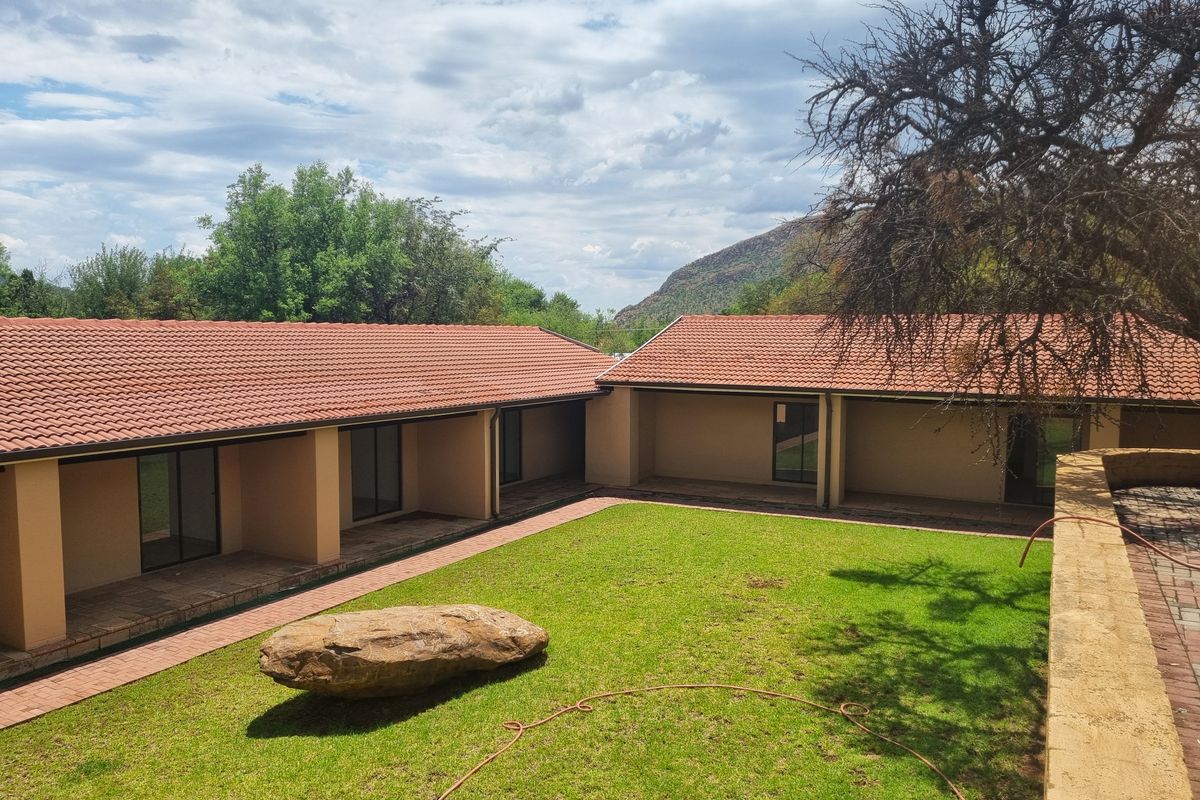 A well-maintained rear exterior view of the guest house featuring a central lawn, covered patio areas, and terracotta tiled roofing.