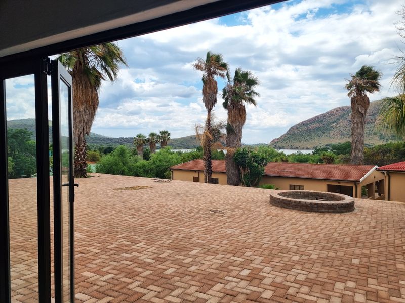 Spacious outdoor patio featuring brick paving and a built-in fire pit, offering scenic views of the surrounding landscape and nearby water.