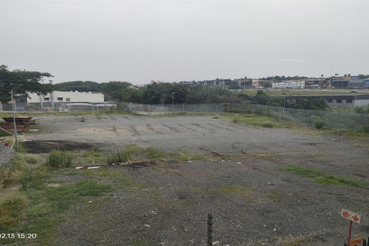 An expansive, undeveloped industrial yard area featuring gravel surfacing and secure perimeter fencing with electric security wires.