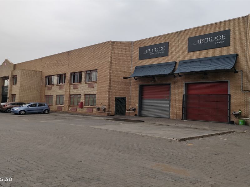 Industrial property exterior featuring a brick facade, multiple roller shutter doors, metal awnings, and a paved driveway area.