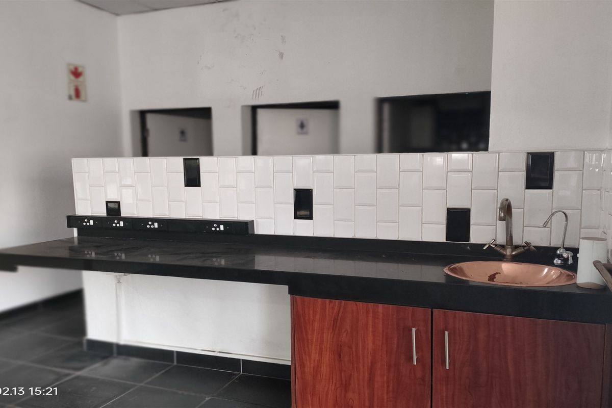 A functional kitchenette area featuring a black stone countertop, subway tile backsplash, copper basin sink, and wood-finish cabinetry.