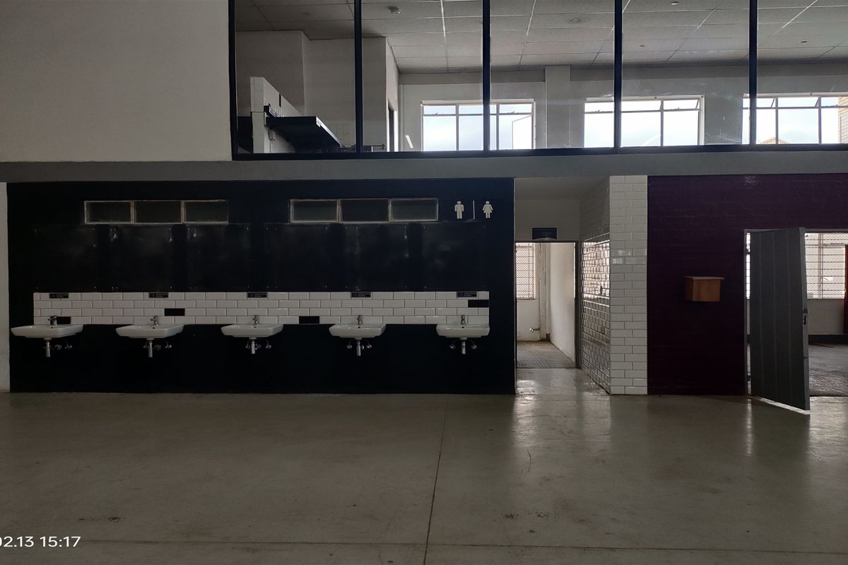 Industrial-style communal washroom area featuring multiple wall-mounted basins, subway tile detailing, and an open-plan layout with mezzanine-level windows.