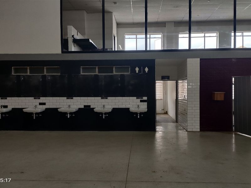 Industrial-style communal washroom area featuring multiple wall-mounted basins, subway tile detailing, and an open-plan layout with mezzanine-level windows.