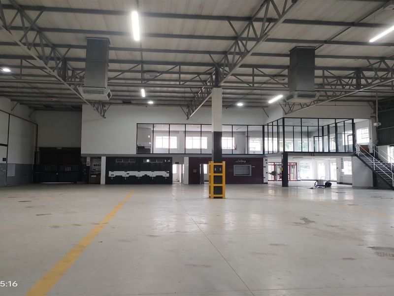 Spacious industrial warehouse featuring high ceilings with exposed steel trusses, concrete flooring, mezzanine office level, and integrated industrial lighting.