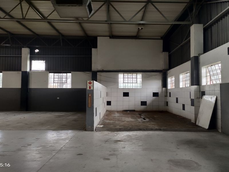 Industrial utility space featuring a dedicated wash bay area with tiled walls, floor drainage, and exposed steel roof trusses.