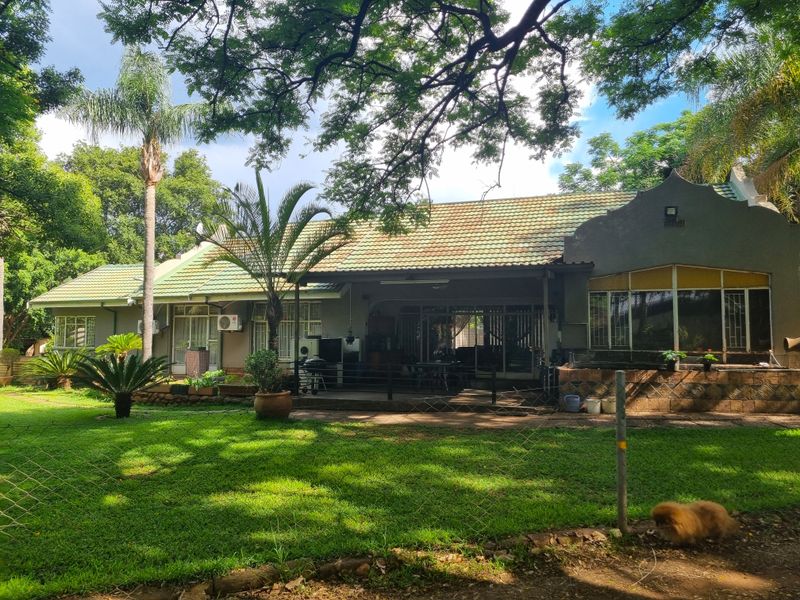 Rear view of a farm-style residence featuring a covered patio, tiled roof, and established garden surroundings.