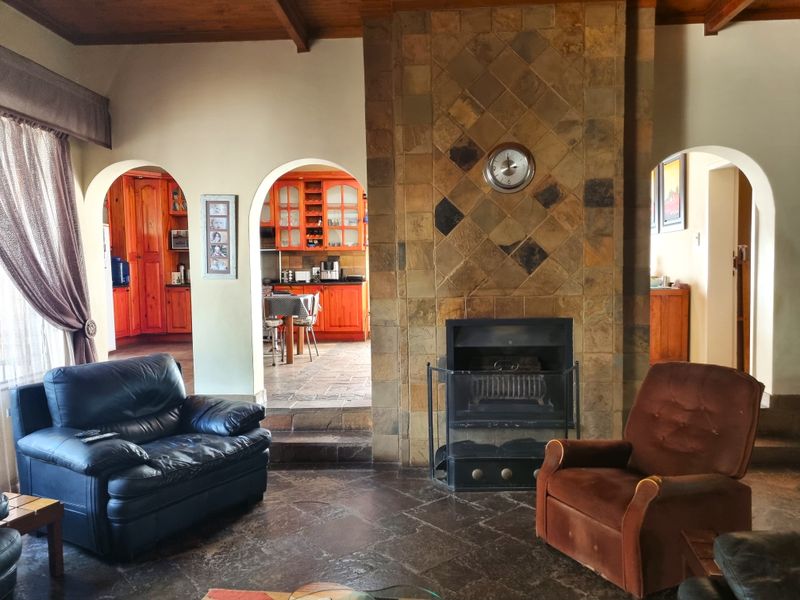 Open plan living area featuring a prominent stone-clad fireplace, timber ceiling, and arched access to a traditional timber kitchen.