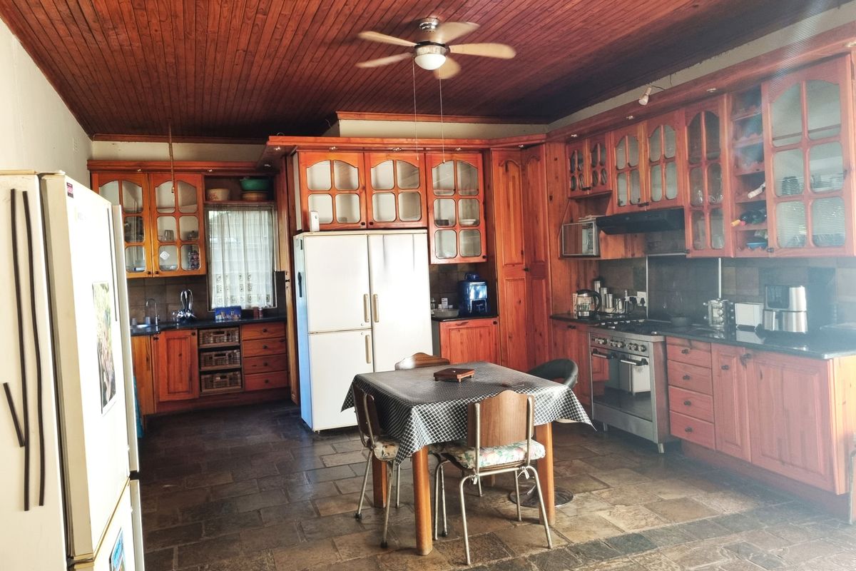 Spacious farmhouse kitchen featuring extensive wooden cabinetry, stone tile flooring, a timber-clad ceiling, and integrated cooking appliances.