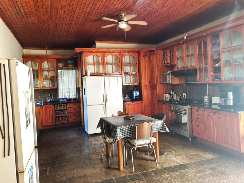 Spacious farmhouse kitchen featuring extensive wooden cabinetry, stone tile flooring, a timber-clad ceiling, and integrated cooking appliances.
