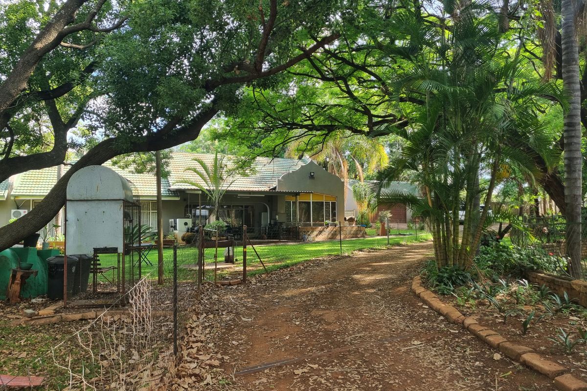 A view of the rear garden and property exterior, featuring mature trees, a lawn, and a rustic driveway approach.