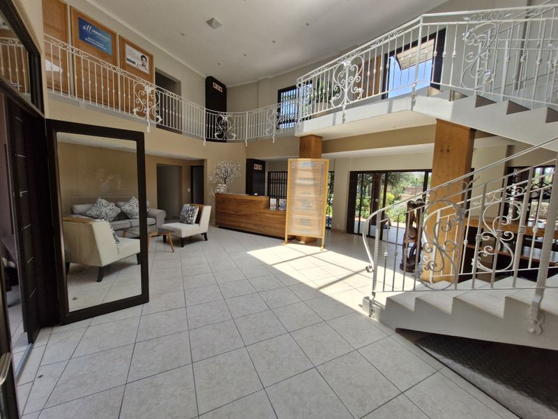 Spacious commercial entrance lobby featuring a grand staircase with wrought iron railings, tiled flooring, and a built-in reception desk.