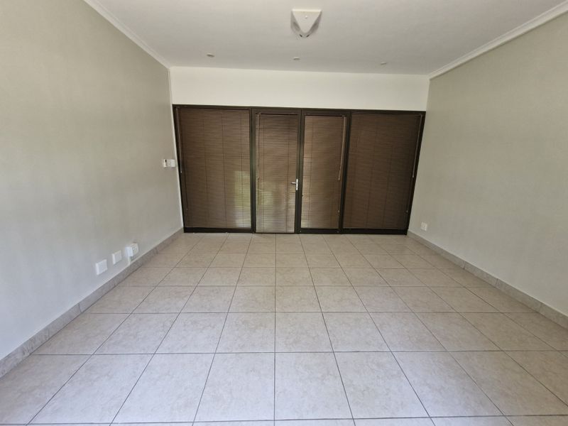 A bright, empty living area featuring neutral tiled flooring, recessed ceiling lighting, and large aluminium sliding doors with fitted venetian blinds.