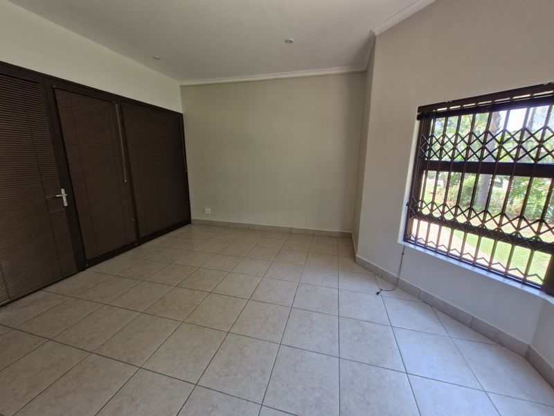 An empty bedroom featuring tiled flooring, built-in cupboards, and a window fitted with a security gate.