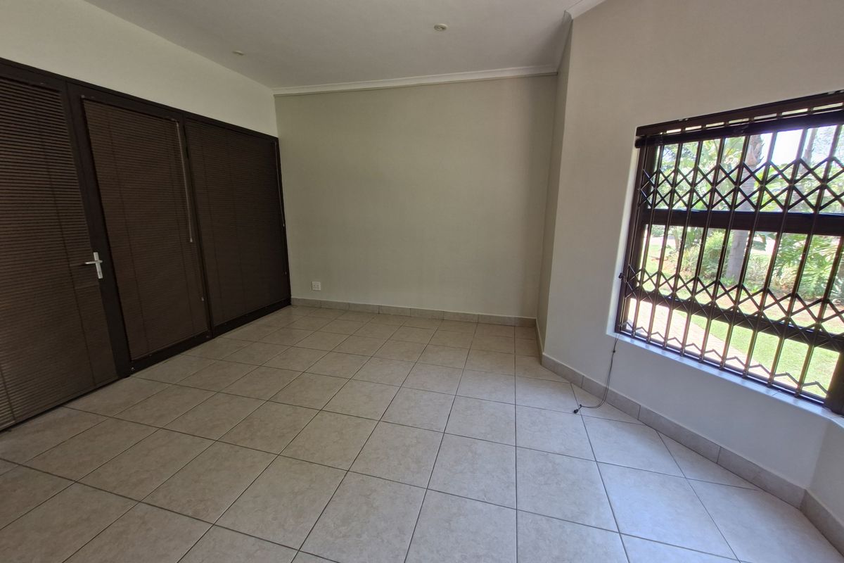 An empty bedroom featuring tiled flooring, built-in cupboards, and a window fitted with a security gate.