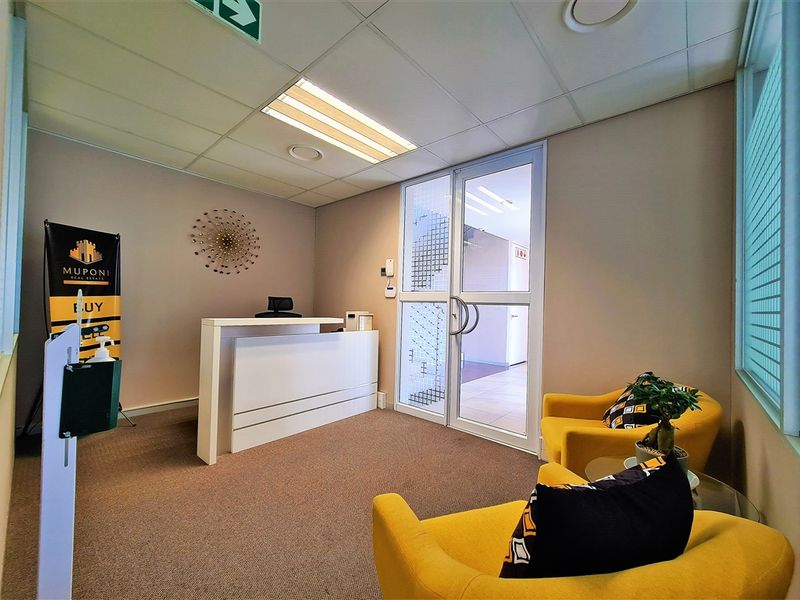 A professional office reception area featuring a built-in reception desk, glass entry door, suspended ceiling, and carpeted flooring.