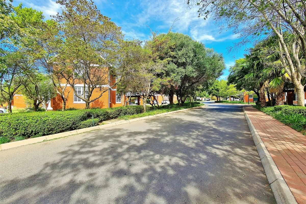 A view of the office park access road featuring mature trees, landscaped garden beds, and paved walkways.
