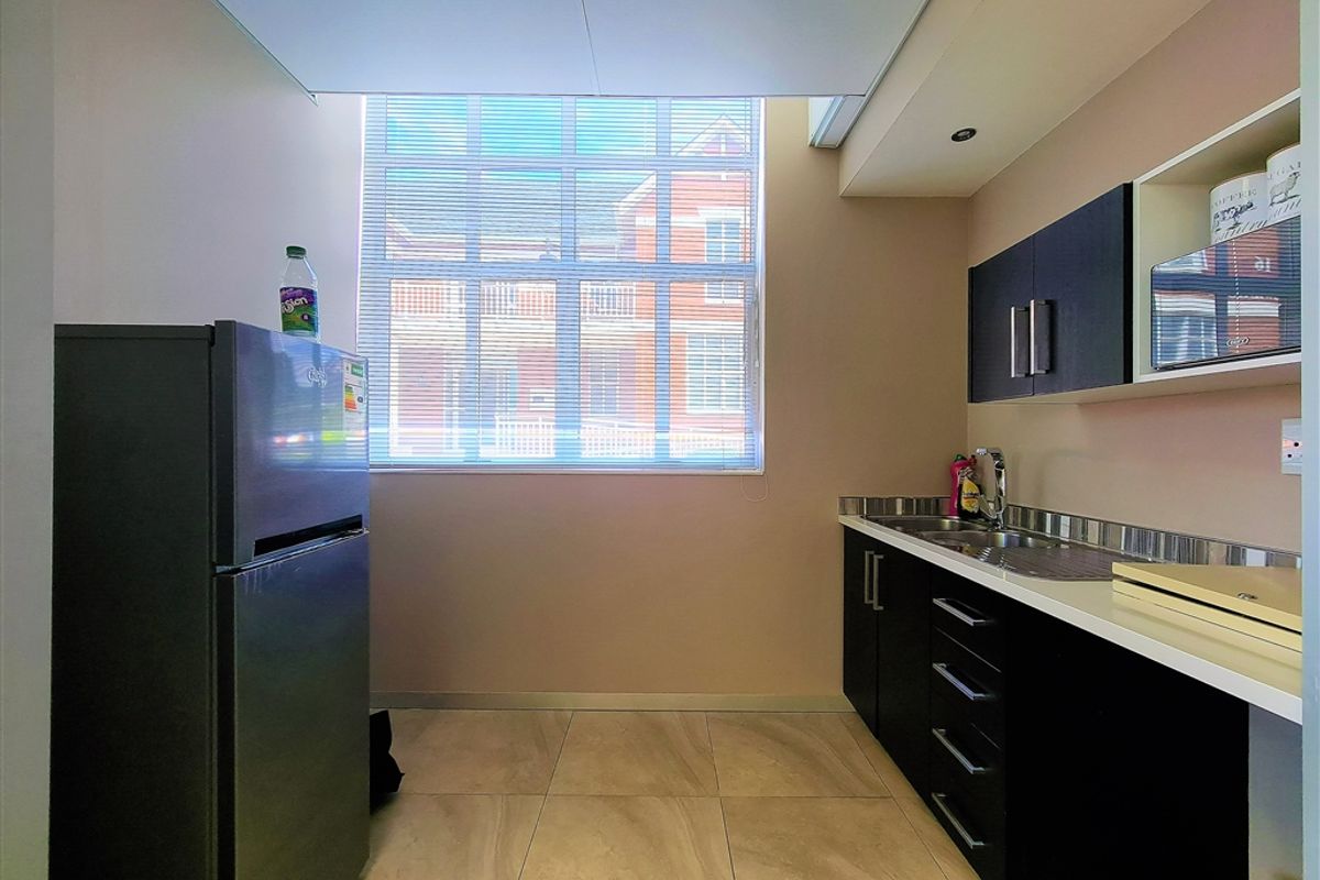 A compact office kitchenette featuring modern dark cabinetry, stainless steel sink, tiled flooring, and a large window providing natural light.
