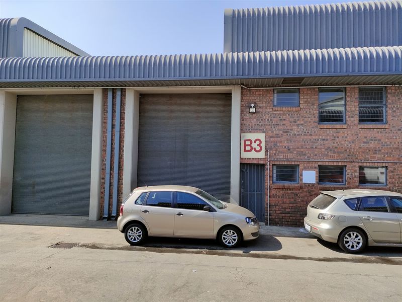 Industrial unit exterior featuring face brick facade, large roller shutter doors, and corrugated metal roofing, providing functional access for commercial or warehouse operations.