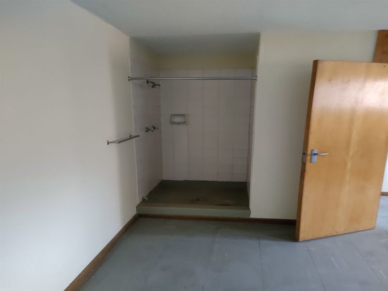 A basic, empty bathroom featuring a walk-in shower stall with tiled walls and a timber door, requiring cosmetic updates to improve its condition.