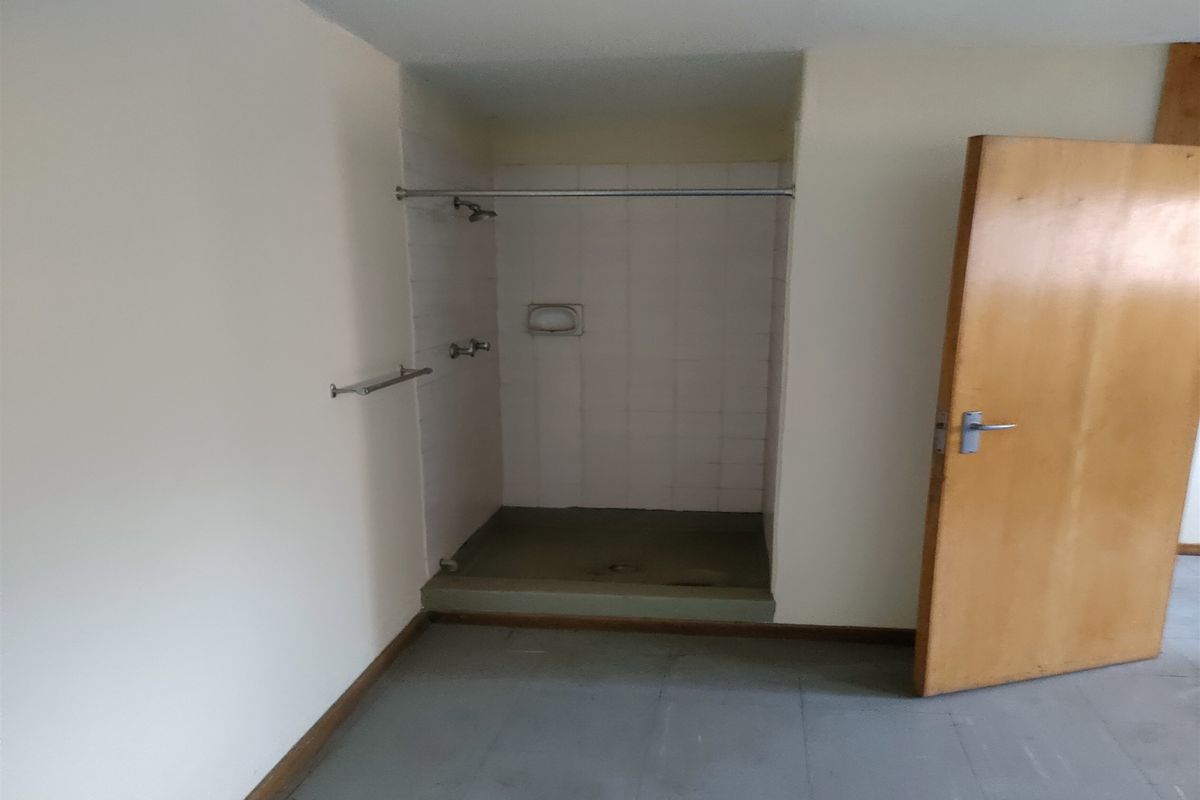 A basic, empty bathroom featuring a walk-in shower stall with tiled walls and a timber door, requiring cosmetic updates to improve its condition.