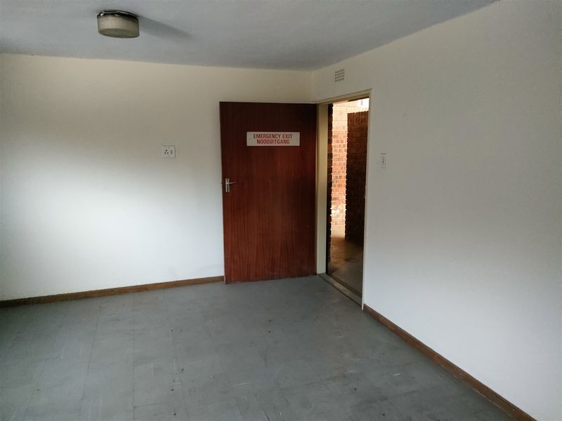 A functional utility space featuring an emergency exit door, vinyl tile flooring, and basic overhead lighting, suitable for storage or administrative use.