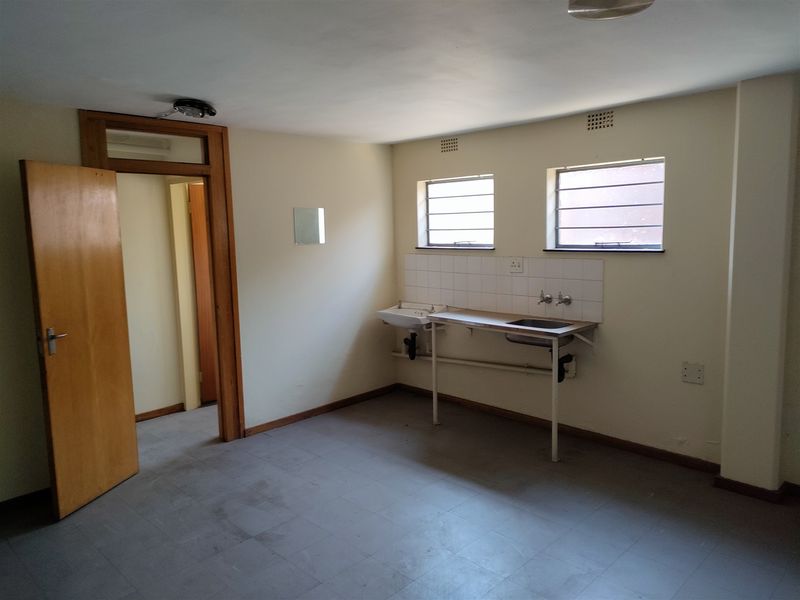 A basic, empty utility kitchen area featuring a stainless steel sink, tiled splashback, and simple metal-framed windows in an industrial property setting.