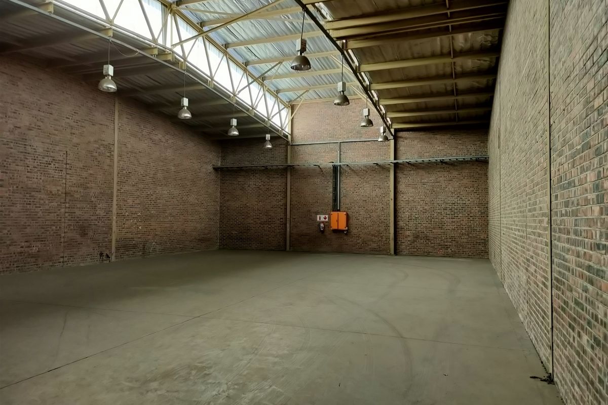 Spacious industrial warehouse unit featuring exposed brick walls, concrete flooring, high truss ceilings with skylights, and functional industrial lighting.