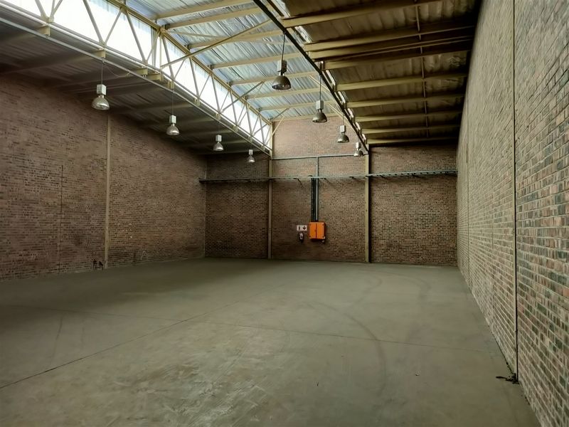 Spacious industrial warehouse unit featuring exposed brick walls, concrete flooring, high truss ceilings with skylights, and functional industrial lighting.