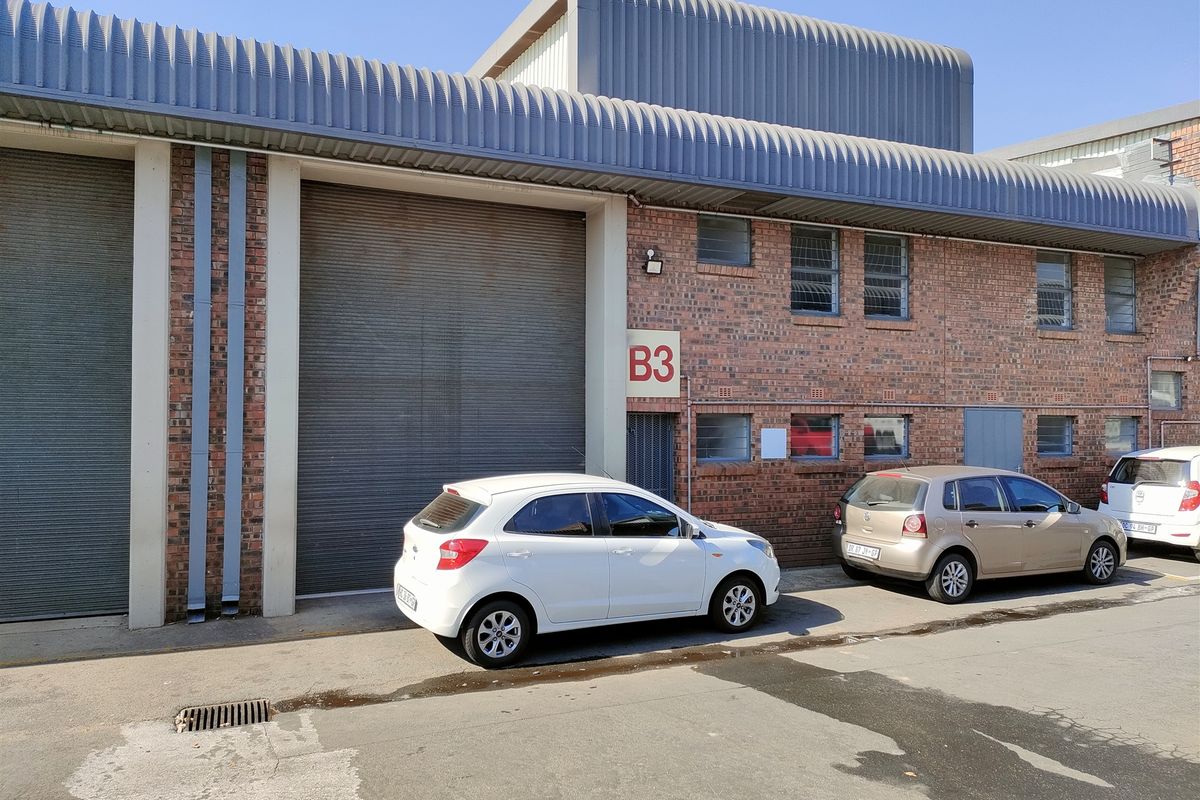 Industrial unit exterior featuring a large roller shutter door, face brick construction, and corrugated metal roofing, providing functional access for commercial operations.
