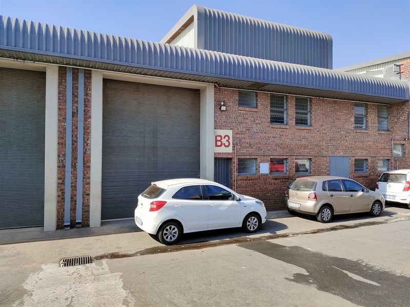 Industrial unit exterior featuring a large roller shutter door, face brick construction, and corrugated metal roofing, providing functional access for commercial operations.