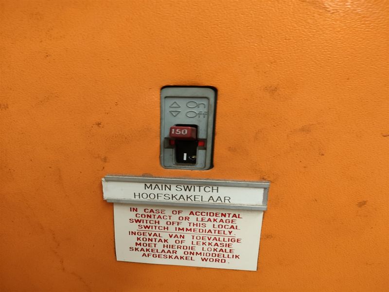 Close-up view of a main electrical switch and safety instruction signage mounted on an industrial orange panel.
