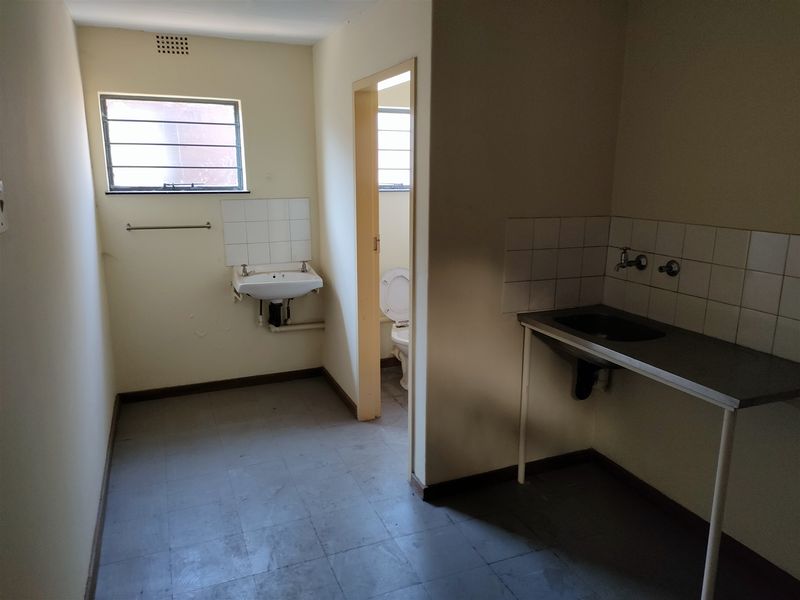 A functional utility or laundry area featuring a stainless steel sink, wall-mounted basin, and an adjoining toilet with basic finishes.