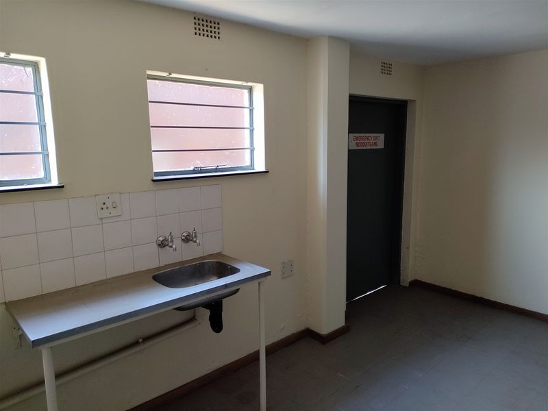 A functional utility space featuring a stainless steel sink, tiled splashback, and a designated emergency exit door, suitable for industrial or commercial use.