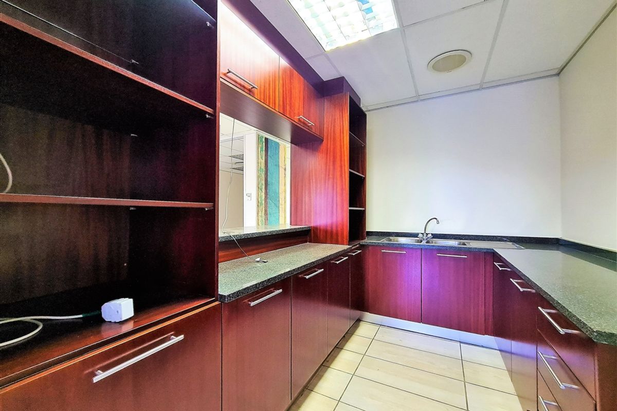 A functional office kitchenette featuring dark wood-veneer cabinetry, stone-look countertops, a stainless steel sink, and integrated shelving.