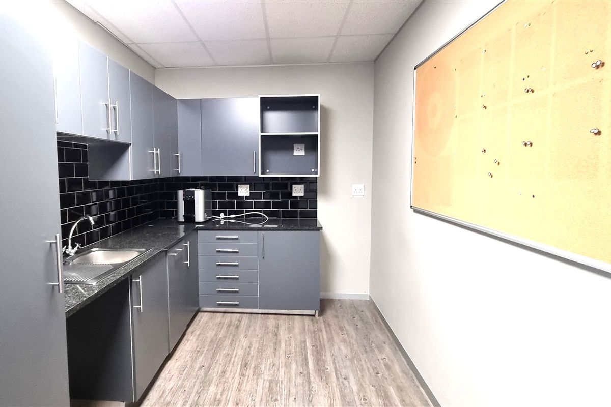 A functional office kitchenette featuring modern grey cabinetry, a dark granite countertop, a stainless steel sink, and a stylish black subway tile backsplash.