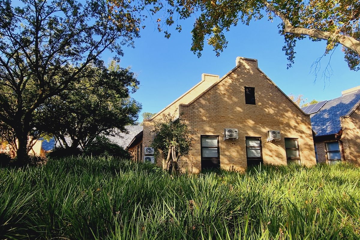 A view of the office building exterior featuring brick facade, mature trees, and landscaped garden surroundings.