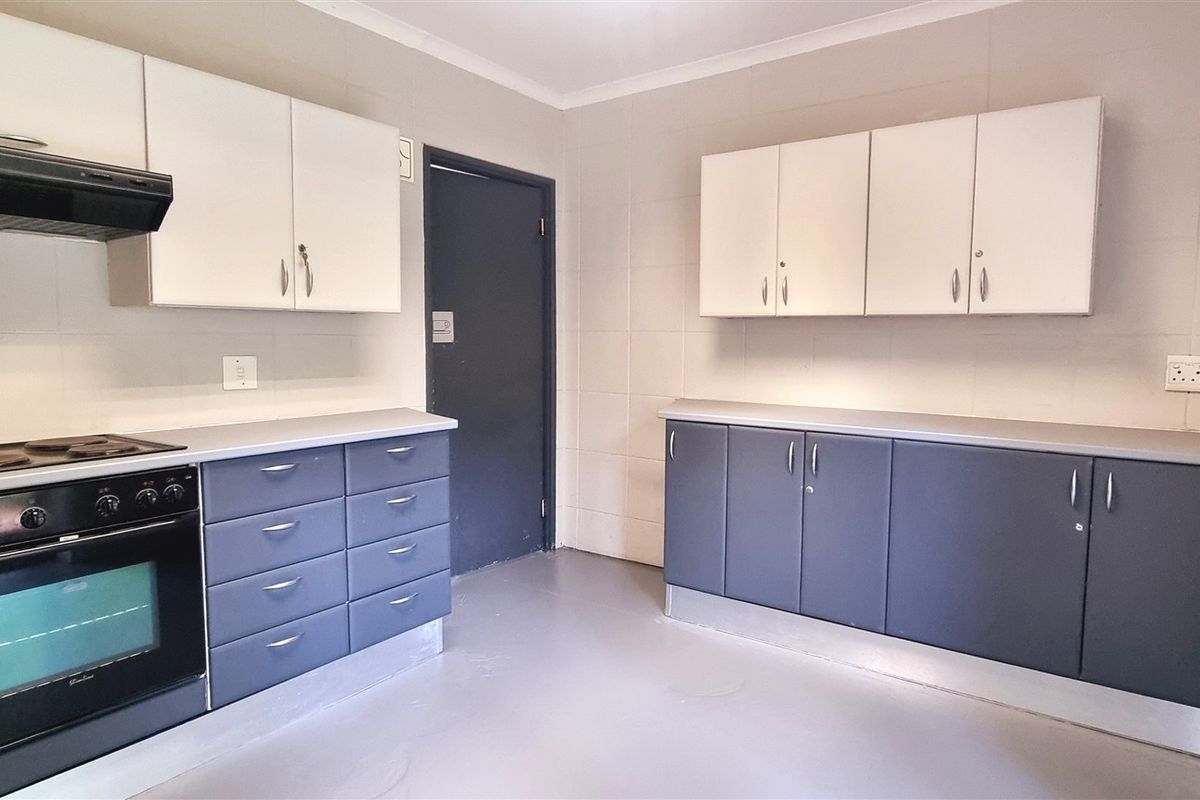 A functional office kitchen area featuring built-in cabinetry, a stove with extractor fan, and tiled wall finishes.