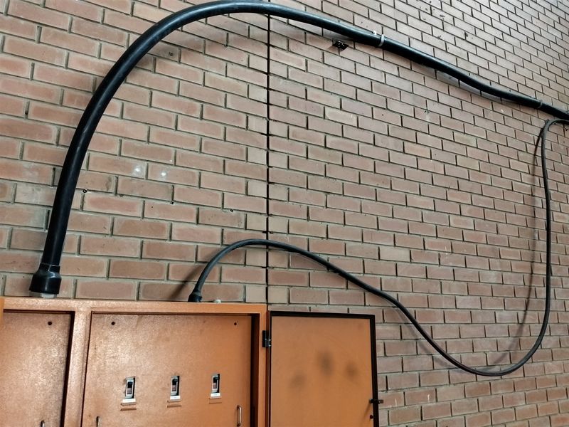 Industrial utility area featuring a wall-mounted electrical distribution board with exposed conduit cabling against a brick masonry wall.