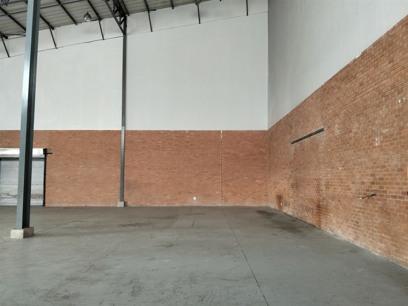 Spacious industrial warehouse unit featuring high ceilings, exposed brick walls, durable concrete flooring, and a secure roller shutter door.