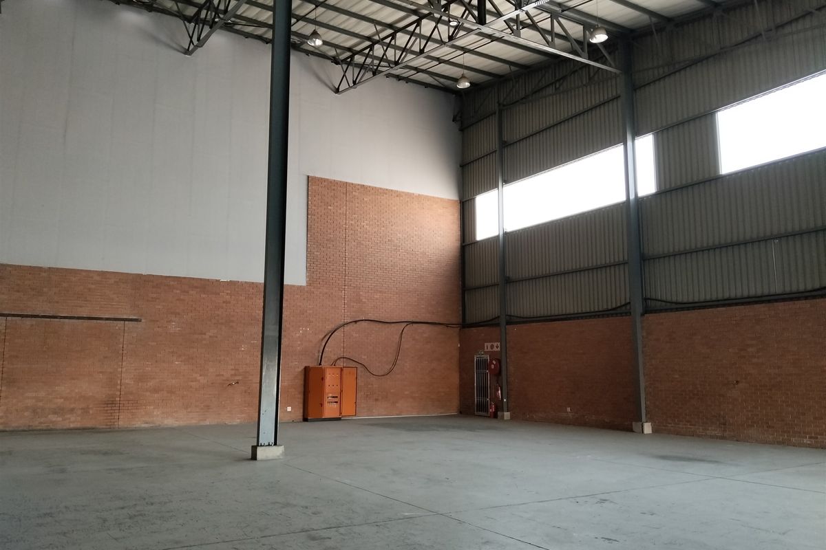 Spacious industrial warehouse unit featuring high ceilings with exposed steel trusses, concrete flooring, and brick wall finishes, suitable for storage or manufacturing operations.