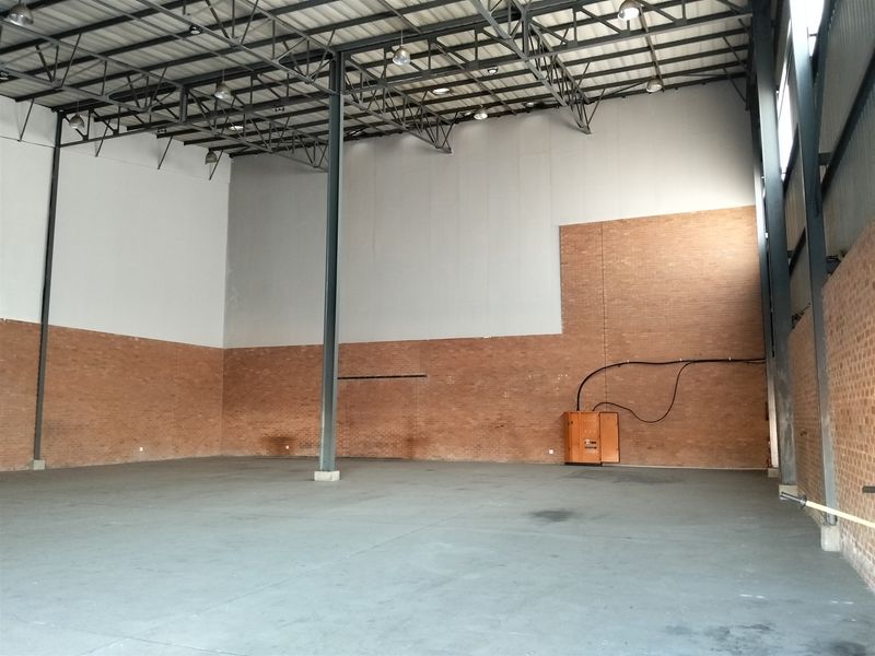 Spacious industrial warehouse unit featuring high ceilings with exposed steel trusses, durable concrete flooring, and exposed brick wall finishes.