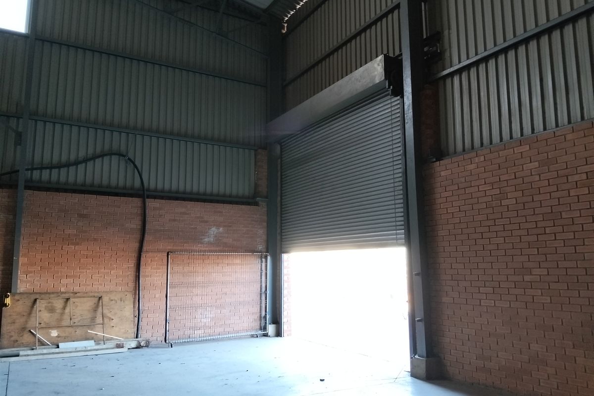 Spacious industrial utility area featuring high ceilings, exposed brick walls, concrete flooring, and a large roller shutter door for vehicle or equipment access.