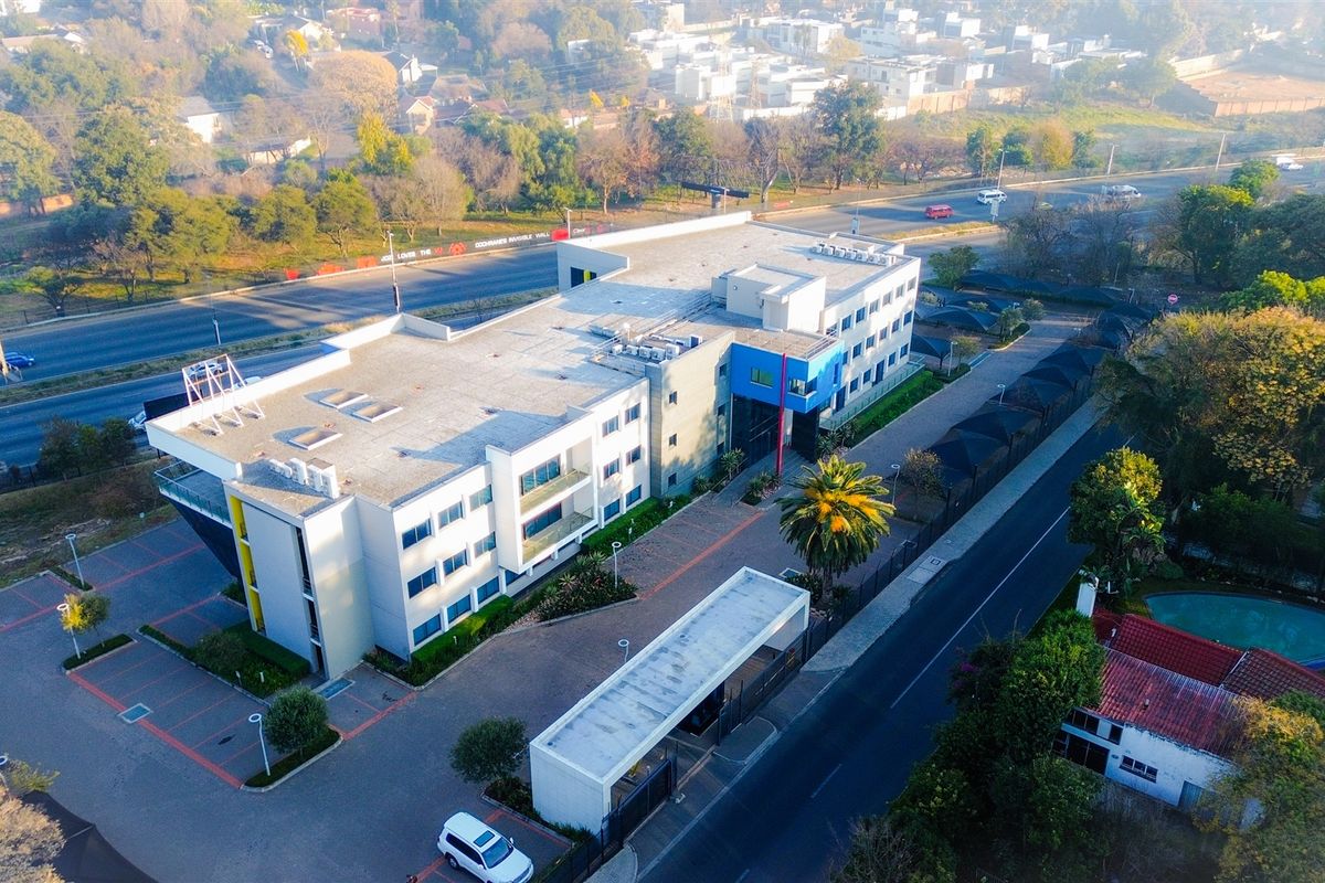 Aerial view of a multi-story office building featuring a paved parking area, secure gated entrance, and landscaped surroundings.