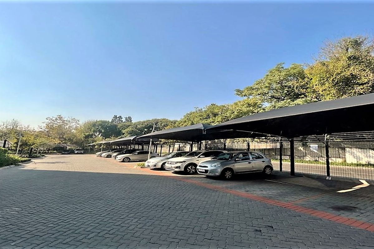 Outdoor parking area featuring paved ground surfaces and covered shade-net parking bays for multiple vehicles.