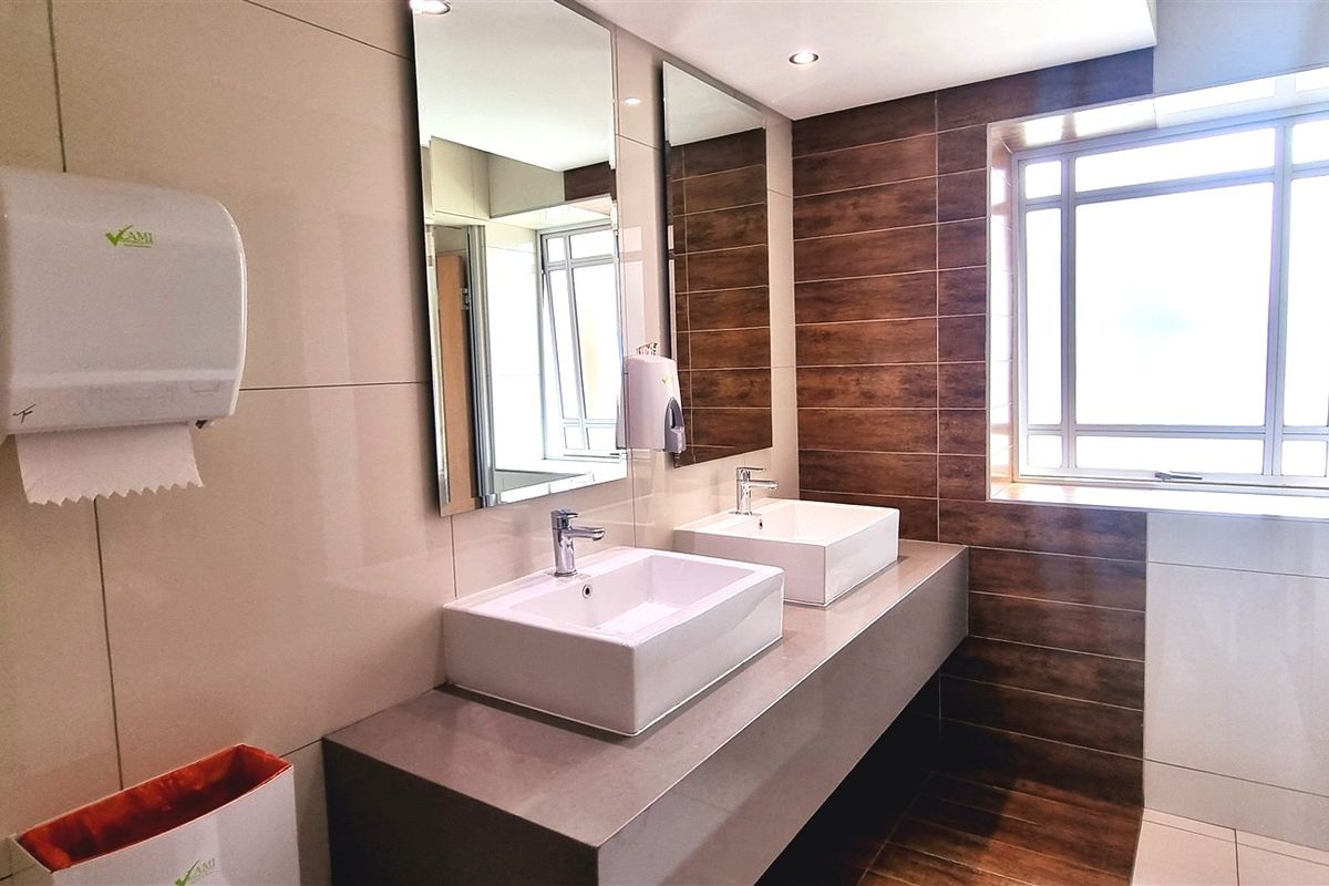 Modern office bathroom featuring a double vanity with vessel sinks, large wall-mounted mirrors, and contemporary wood-look and neutral ceramic tiling.