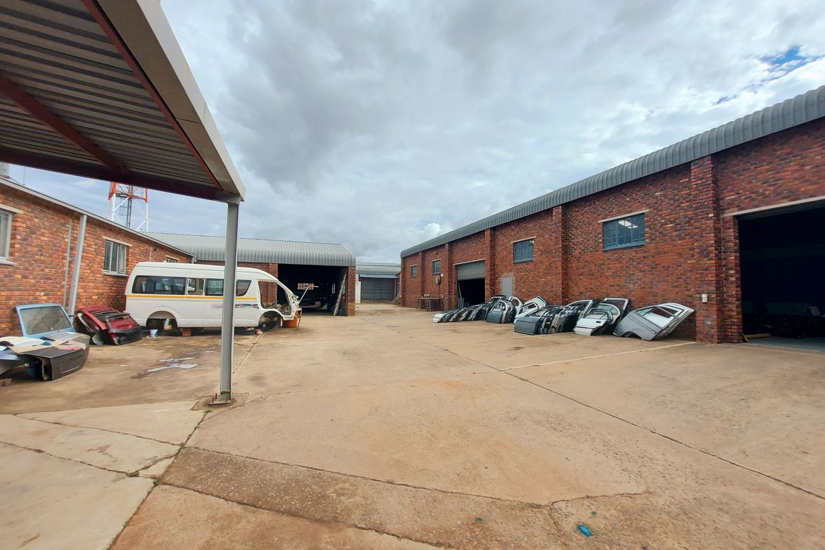 Industrial yard area featuring brick warehouse buildings with large roller shutter doors and a covered loading bay.