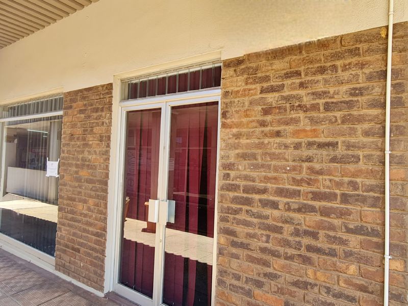 Front exterior view of an office unit featuring a brick facade, aluminium framed glass entrance doors, and large display windows under a covered walkway.