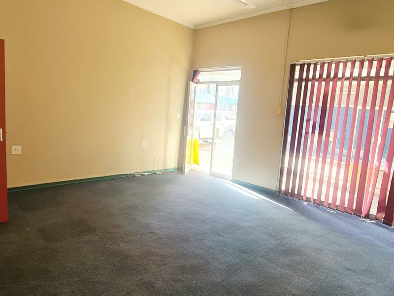 An empty office space featuring dark carpet flooring, vertical window blinds, and a glass panel door providing natural light.